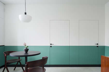 Modern dining room with dark table and chairs, simple ceiling lamp and decorative wall and doors half white and greenの写真素材