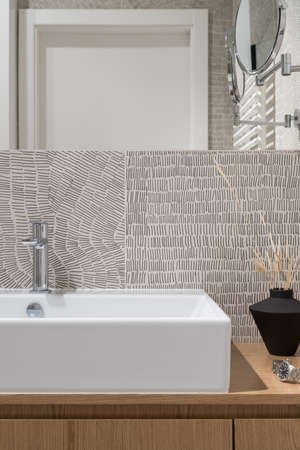 Close-up on classic white washbasin in wooden cabinet with decorations in modern bathroom with stylish and patterned wall tilesの写真素材
