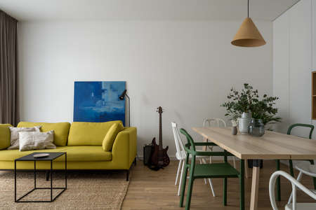 Apartment with modern and stylish living room with comfortable, yellow sofa and nice black coffee table and dining area with wooden table and different chairsの写真素材