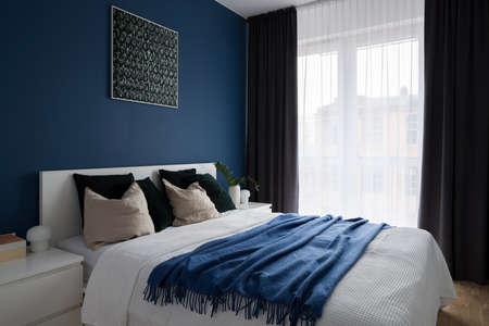 Comfortable bedroom with double bed, big window and modern blue wallの写真素材