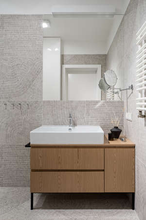 Stylish and modern bathroom with decorative and patterned floor and wall tiles, elegant white washbasin with wooden cabinet and big mirrorの写真素材