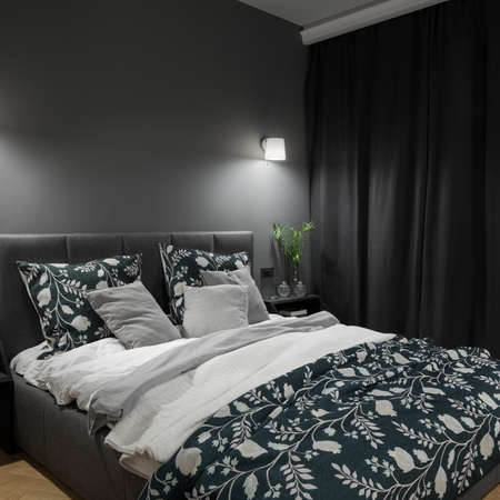 Big and comfortable bed in stylish and dark bedroom with gray walls, curtains and nice lightingの写真素材
