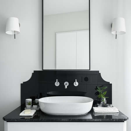 Close-up on stylish bathroom washbasin on white cabinet with black countertop and big mirrorの写真素材