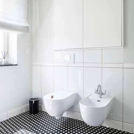 Close-up on stylish bidet and toilet in modern bathroom with black and white mosaic tiles on the floorの写真素材
