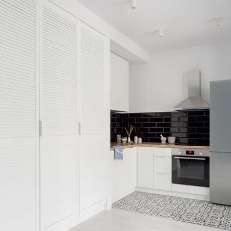Small and stylish kitchen in black and white with big white wardrobe in bright studio apartmentの写真素材