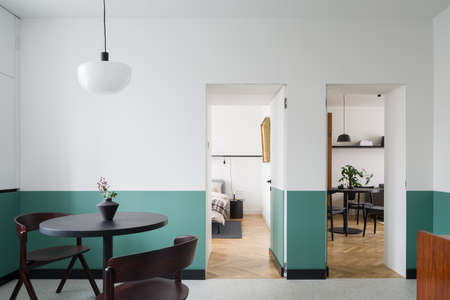 Modern designed dining area with black, round table and stylish, dark chairs under simple pendant lamp in room with white and green walls and doors open to living room and bedroomの写真素材