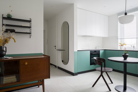 Vintage, wooden sideboard in modern green and white kitchen with terrazzo floor and black dining tableの写真素材
