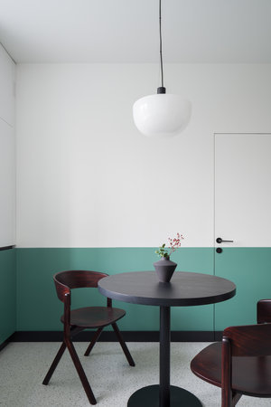 Stylish, round, wooden dining table with two modern chairs under new lamp in room with decorative white and green wall and terrazzo floorの写真素材