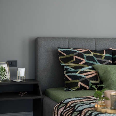 Close-up on comfortable bed with colorful bedclothes and simple, black bedside table with decorationsの写真素材