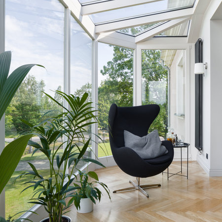 Stylish room with nice oriel window and relax area with black chair, houseplants and tableの写真素材