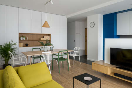 Simple and modern dining table with colorful and different chairs in stylish living room with tv open to kitchen areaの写真素材