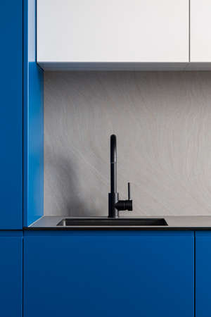 Close-up on modern black kitchen tap and sink in kitchen with stylish navy blue and white cupboards and gray countertop and backsplashの写真素材