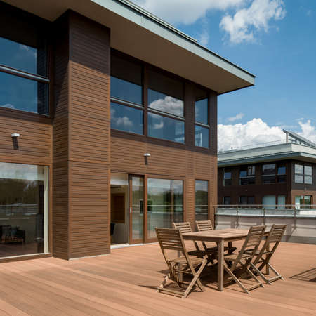 Spacious terrace with wooden floor, chairs and table in modern residential building, exterior viewの写真素材
