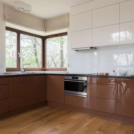 Spacious and modern kitchen with wooden floor, big window and brown and white furnitureの写真素材