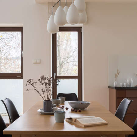 Bright dining room with fancy chandelier above long, wooden table with nice decorations and black chairsの写真素材