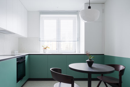 Modern kitchen half white and half green and with black dining table with two chairs and new lamp aboveの写真素材