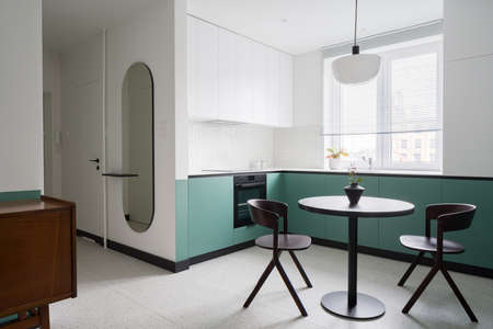 Stylish apartment with modern white and mint kitchen with black dining table and chairs open to corridor with trendy oval mirrorの写真素材