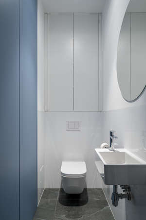Contemporary design in bathroom with white and blue walls, big round mirror, simple and small white washbasin and toiletの写真素材