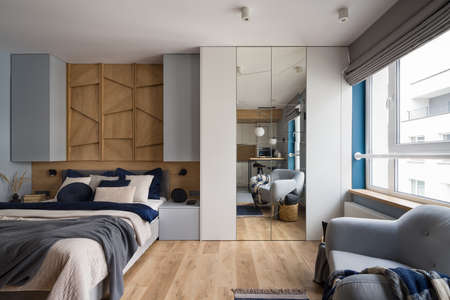 Stylish studio apartment with big window, comfortable bed, big wardrobe with mirror and cozy armchairの写真素材