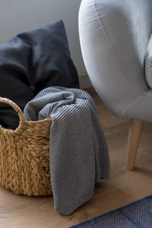 Close-up on decorative wicker basket with dark pillow and gray blanket next to gray armchairの写真素材