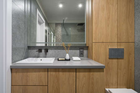Modern design in bathroom with white square washbasin, big mirror, wooden chest of drawers, cabinets and terrazzo tilesの写真素材