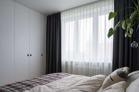 Bright bedroom with king size bed, big window with stylish curtains and wardrobe with white doorsの写真素材