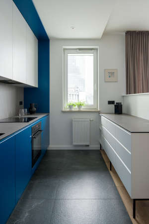 Modern and narrow kitchen with window and stylish white and blue cupboardsの写真素材
