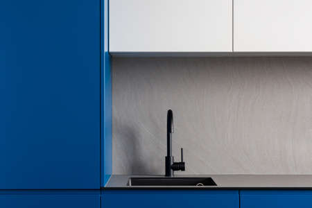 Elegant and simple black sink and tap in modern kitchen with blue and white cupboards and stylish gray countertopの写真素材