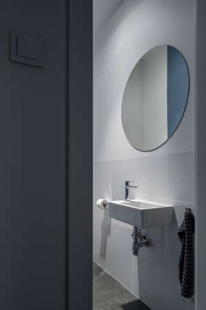 Big, round mirror above small white washbasin in bright bathroom with gray tilesの写真素材
