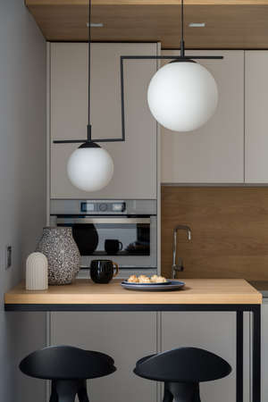 Small kitchen with decorative lamps, white furniture and wooden table with two chairsの写真素材