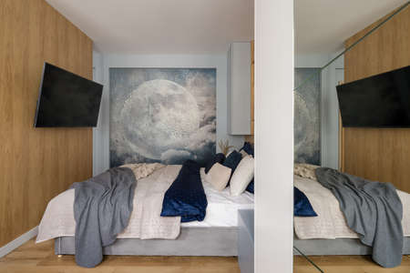 Small bedroom with big and comfortable bed and tv on wooden wall and wallpaper with moonの写真素材