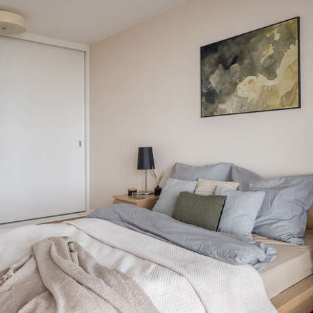 Bright bedroom with art, king size bed, wooden bedside table with black lamp and big wardrobeの写真素材