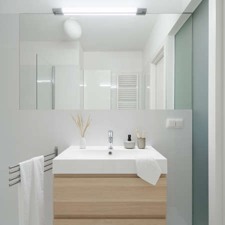 Simple washbasin with wooden cabinet with drawers under big mirror in lavatory with frosted glass on wallの写真素材