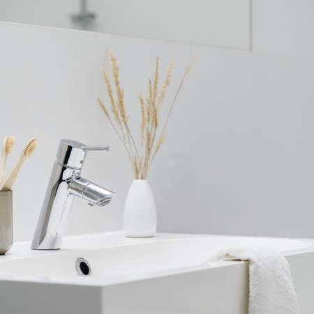 Close-up on bathroom washbasin with silver tap, towel, decorative vase with grass and two toothbrushの写真素材