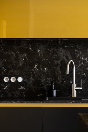 Silver tap in black sink in modern kitchen with black and gold cupboards and marble style backsplashの写真素材