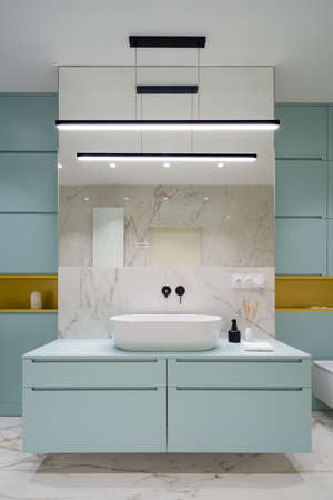 Modern bathroom with blue cabinets and drawers under new washbasin, led lighting, big mirror and elegant marble style floor and wall tilesの写真素材
