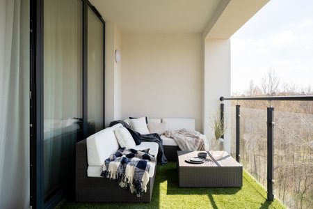 Cozy decorated balcony with big window doors to apartment, synthetic grass and stylish rattan corner sofa with decorative pillows and rattan coffee tableの写真素材