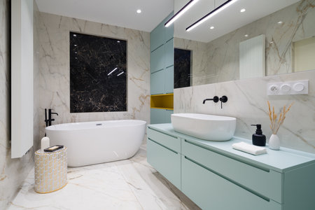 Elegant bathroom with freestanding bathtub and blue chest with drawers under washbasin, blue cabinets and marble tilesの写真素材