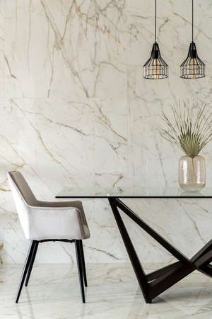 Elegant, gray chair and modern dining table with glass top in stylish room with marble tiles on wall and floorの写真素材