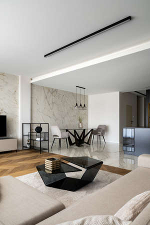 Stylish dining area with modern table with two chairs in open and elegant living room with wooden floor, marble wall and new, black coffee tableの写真素材