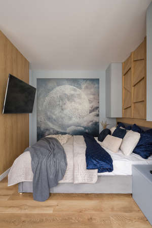 Small and stylish bedroom with moon wall mural, tv on wooden wall and cozy and nice decorated bedの写真素材