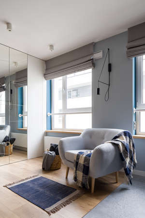 Comfortable armchair with decorations in bright room with big windows and wardrobe with mirror doorの写真素材
