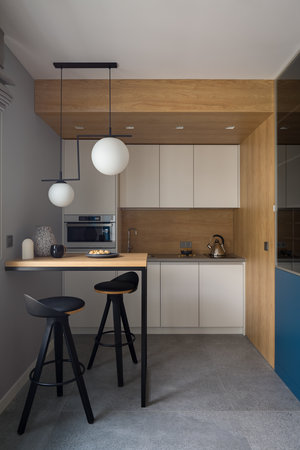 Small and modern kitchen with white furniture, wooden walls and table with two, black chairs and granite floor tileの写真素材