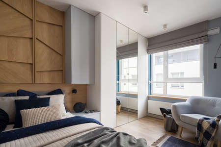 Spacious bedroom with comfortable bed with nice bedclothes, big window, wardrobe with mirror and armchairの写真素材