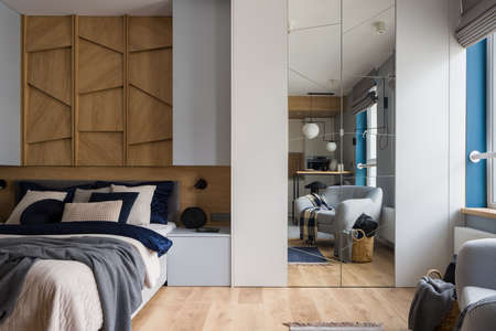 Open bedroom with cozy bed and wooden wall decor in stylish studio apartmentの写真素材