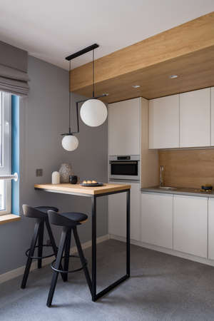 Stylish kitchen with white furniture, granite floor tiles and small table for two under modern pendant lampsの写真素材