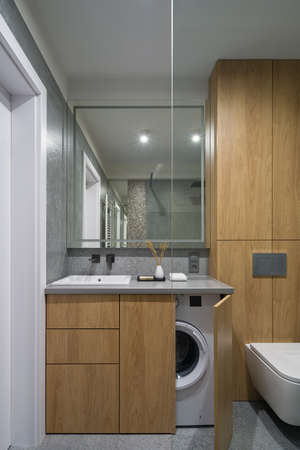 Modern and functional bathroom with wooden furniture and wall and granite floor and wall tiles and washing machine in cabinetの写真素材