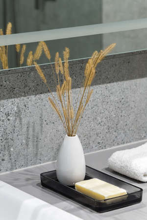 Close-up on decorative white vase with dried grass and natural soap bar on tray next to white towel in bathroom with granite tilesの写真素材