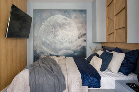 Small bedroom with wooden walls, comfortable bed with nice bedclothes and decor and big tv screen and poster with moonの写真素材