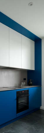 Vertical panorama of modern designed kitchen with stylish blue walls and cupboards, gray countertop and backsplash and white upper cabinetsの写真素材